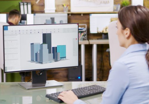 Female architect making 3d building models on computer. Architect holding blueprint.